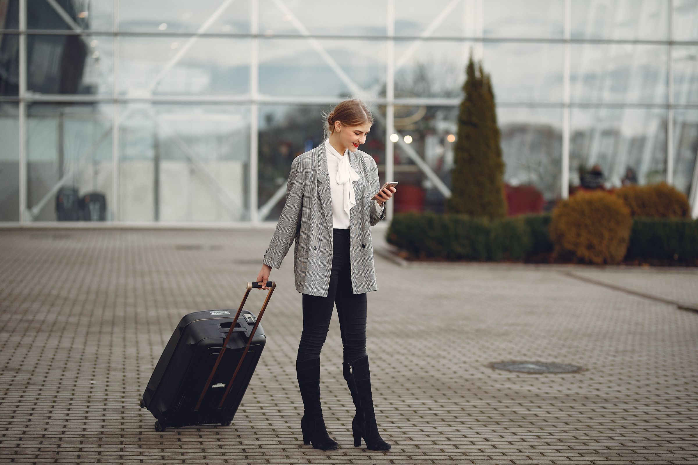 Business traveller using a phone with luggage outside an airport